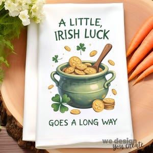May include: White kitchen towel with the text "A LITTLE, IRISH LUCK GOES A LONG WAY." The towel features a green pot filled with gold coins, a wooden spoon, and shamrocks. Carrots and flowers are in the background.