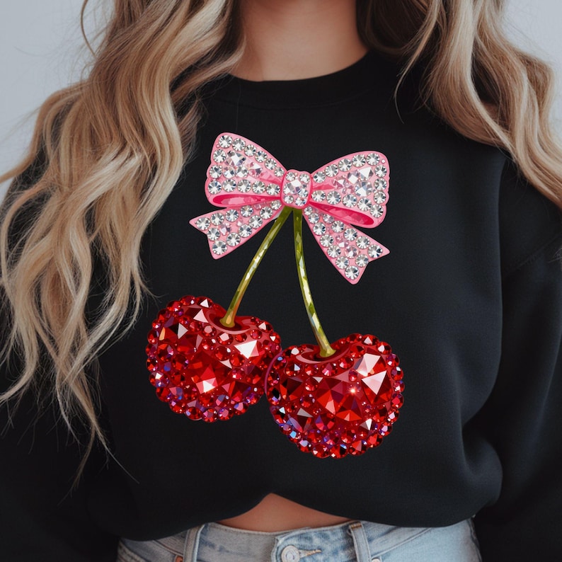 May include: Black sweatshirt featuring a pink bow with crystal embellishments and two red crystal-covered cherries. The cherries have green stems. The design is centered on the front of the sweatshirt.
