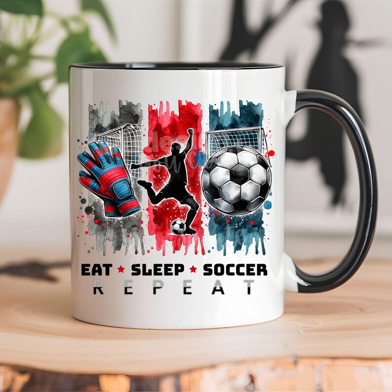 May include: White ceramic mug with a black handle. The mug features a watercolor design of a soccer player, a soccer ball, and a pair of goalie gloves. The text "Eat Sleep Soccer Repeat" is printed on the mug.