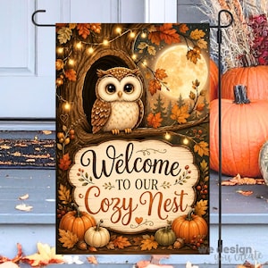 May include: A rectangular garden flag featuring a brown owl perched in a tree hollow, surrounded by autumn leaves, string lights, and a full moon. Below, a wooden sign reads Welcome TO OUR Cozy Nest, with orange pumpkins at the base.