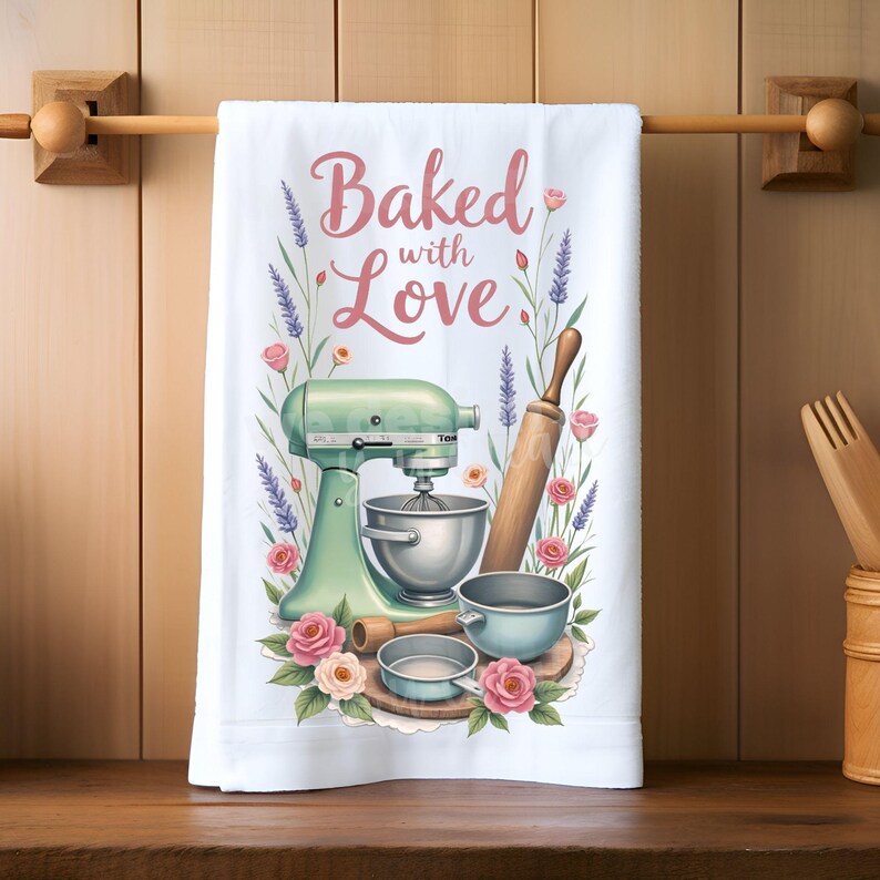 K&ouml;nnte beinhalten: Wei&szlig;es K&uuml;chentuch mit einem Design "Baked with Love". Die Illustration zeigt einen mintgr&uuml;nen K&uuml;chenmixer, eine Teigrolle, R&uuml;hrsch&uuml;sseln und florale Akzente in Rosa und Lila. Das Handtuch h&auml;ngt an einer Holzstange.
