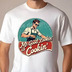 Peut inclure: T-shirt blanc avec un graphisme r&eacute;tro d'un homme portant des lunettes de soleil et un tablier, en train de cuisiner. Le texte dit "Mr Good Lookin' is Cookin'".