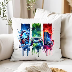 May include: A white pillow with a colorful watercolor design featuring a video game controller, headphones, and a game console. The design is in shades of blue, green, red, and yellow.