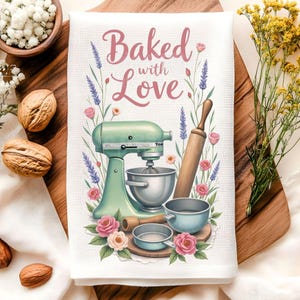 K&ouml;nnte beinhalten: Wei&szlig;es K&uuml;chentuch mit einer Aquarellillustration eines mintgr&uuml;nen K&uuml;chenmixers, einer Teigrolle und R&uuml;hrsch&uuml;sseln. Der Text "Baked with Love" ist in rosa Schrift geschrieben, umgeben von Blumen und Lavendelzweigen.