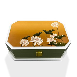 May include: A wooden jewelry box with a green base and a white lid. The lid features a gold and orange gradient background with a white lotus flower design.