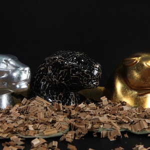 May include: Three panther figurines, one silver, one black with gold accents, and one gold. The figurines are sitting on a bed of wood shavings.