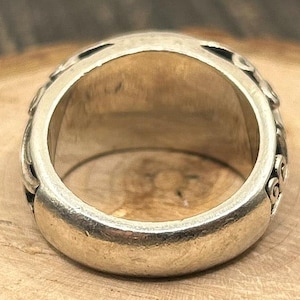 May include: A silver ring with intricate designs on the band. The ring is wide and has a smooth, rounded surface.