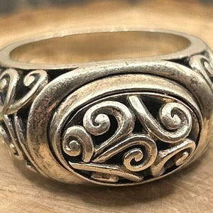 May include: A silver ring with a detailed swirl design. The ring is made of metal and has a smooth finish.