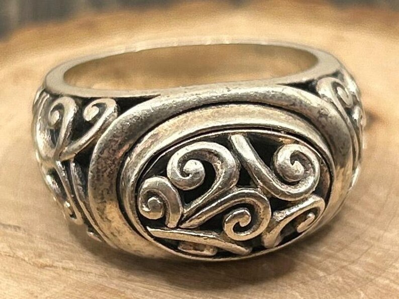 May include: A silver ring with a detailed swirl design. The ring is made of metal and has a smooth finish.