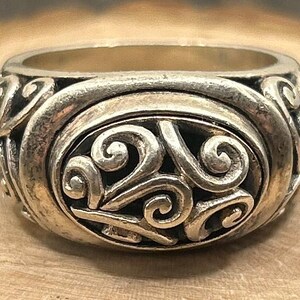 May include: A silver ring with a detailed swirling design. The ring is made of metal and has a smooth, polished finish.