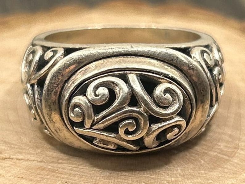 May include: A silver ring with a detailed swirling design. The ring is made of metal and has a smooth, polished finish.
