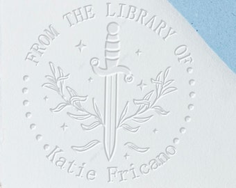May include: A white stamp with the text "From the Library of Katie Friciano" in a circle around a sword with leaves and stars.