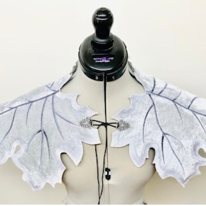 Puede incluir: Un collar de terciopelo plateado en forma de hoja con cierres de metal plateado. El collar está en un maniquí blanco.