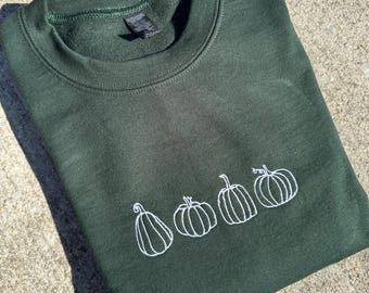 May include: A dark green sweatshirt with a white embroidered design of four pumpkins.