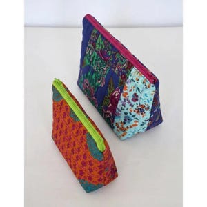 May include: Two quilted cosmetic bags. One is orange with a geometric pattern and a lime green zipper. The other is blue with floral and patterned fabric panels and a pink zipper. Both are triangular in shape.