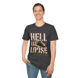 May include: A dark gray short-sleeve t-shirt featuring a graphic print of a helicopter in flight with flames and soldiers below. The text HELL LET LOOSE is printed in large white letters above the word VIETNAM in smaller olive green text.