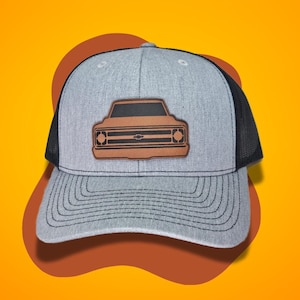 May include: A gray and black trucker hat with a brown leather patch featuring a vintage truck silhouette.