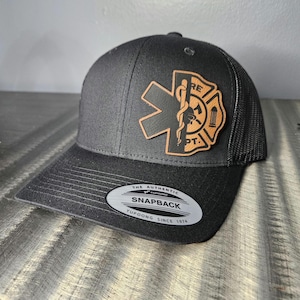 May include: Black trucker hat with a brown leather patch featuring a combination of a medical star of life and a fire department symbol. The patch reads "Fire Dept.". The hat has a black mesh back and a black YUPOONG snapback closure with the text "The Authentic Yupoong Snapback Yupoong Since 1974".