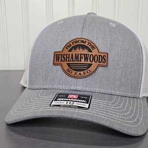 May include: Gray and white trucker hat with a brown leather patch that says "I'm from the Wishamfwoods So F.A.F.O.". The patch has a silhouette of trees and a black stripe. The hat is adjustable and has a Richardson 112 label.