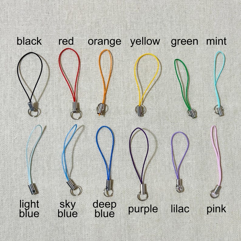 May include: A collection of colorful phone charms in black, red, orange, yellow, green, mint, light blue, sky blue, deep blue, purple, lilac, and pink. Each charm has a loop and a metal clasp, with color names labeled below.