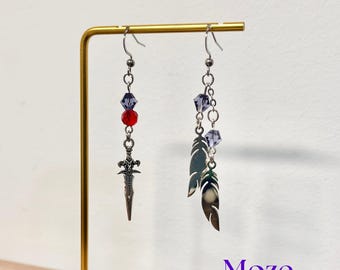 May include: A pair of dangle earrings with a unique design. One earring features a small silver dagger charm, red and purple beads. The other earring has silver feather charms and purple beads. The earrings are displayed on a gold stand.
