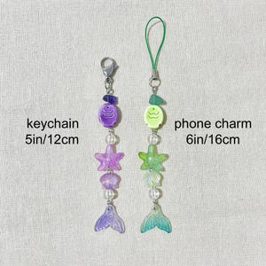 May include: Two beaded mermaid-themed accessories: a keychain (5 inches/12 cm) and a phone charm (6 inches/16 cm). The keychain features purple beads, a starfish, a shell, and a mermaid tail. The phone charm has green beads, a starfish, a shell, and a mermaid tail.