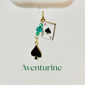 May include: A gold-colored charm with a black spade and an Ace of Spades playing card design, accented with teal beads. The word "Aventurine" is printed in green at the bottom.