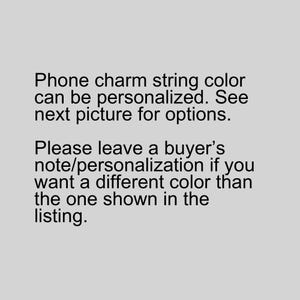 May include: Text on a gray background states that the phone charm string color can be personalized. It directs the buyer to the next picture for options and to leave a note if a different color is desired.