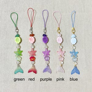 May include: Five colorful mermaid-themed charms with matching loops. Each charm features a fish, starfish, shell, and mermaid tail in green, red, purple, pink, and blue. The word labels are green, red, purple, pink, and blue.