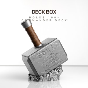 Op de afbeelding: Een hamer-vormige deck box in grijs met een bruin handvat en zilveren knop. De zijkant bevat de gegraveerde tekst "Whosoever holds this hammer, if he be worthy, shall possess the power of THOR". De tekst erboven luidt "DECK BOX" en "HOLDS 100+ COMMANDER DECK".