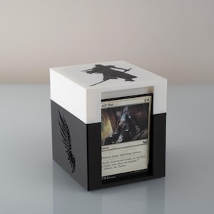 May include: A black and white card storage box with a card visible inside. The box has a white top with a black silhouette design and a black base with a wing design. The card reads "Kill Shot".