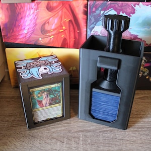 May include: Two black card storage boxes with a screw-on top. One box holds a card with a woman illustration. The other box has a sticker with a blue-haired anime character. The boxes are on a wooden surface.