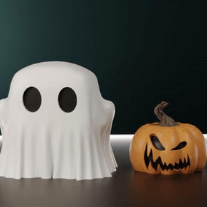 May include: A white ghost figurine with two large black circular eyes and a draped sheet appearance positioned next to an orange pumpkin with a carved, jagged, toothy grin and a brown stem, both displayed on a dark, smooth surface.