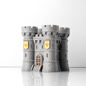 Puede incluir: Un modelo de castillo gris con cuatro torres almenadas, una puerta central arqueada con puertas de madera marrón y dos escudos blancos con emblemas de flor de lis dorados en las torres frontales. La estructura tiene textura de ladrillo.