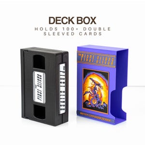Könnte beinhalten: Zwei Kartenboxen, eine schwarze und eine lila. Die schwarze Box ähnelt einer VHS-Kassette. Die lila Box hat eine farbenfrohe Illustration und den Text "THE FIRST SLIVER". Beide Boxen fassen über 100 doppelt geschützte Karten.