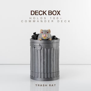 Könnte beinhalten: Eine graue Deckbox in Form eines Mülleimers, mit einer Cartoon-Ratte, die aus der Oberseite herausschaut. Der Text "DECK BOX" und "HOLDS 100+ COMMANDER DECK" sind über der Box aufgedruckt. Der Text "TRASH RAT" ist darunter gedruckt.