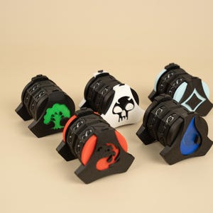 May include: Six black and coloured counter wheels with different symbols. The symbols include a tree, a skull, a diamond, a teardrop, and a dragon. The wheels are numbered 0-9.