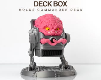 May include: A gray deck box with a pink brain-like figure in a robotic frame. The figure has yellow eyes and a menacing expression. The text "DECK BOX" and "HOLDS COMMANDER DECK" are printed above the figure.