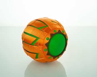 May include: A spherical, orange and green decorative object with a textured surface. The object has a woven pattern with green accents and a circular green center. Small green dots and brown accents are also visible.