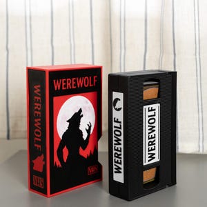 May include: Two decorative boxes, one red and one black, designed to resemble VHS tapes. The red box features a werewolf silhouette howling at a full moon, with the word "WEREWOLF" in white. The black box also has "WEREWOLF" in white.