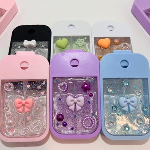 May include: Six small, clear plastic bottles with colourful glitter and charms inside. The bottles are in different colours: pink, purple, blue, white, black, and green. Each bottle has a small bow, hearts, stars, and pearls inside.