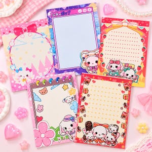 Peut inclure: Cinq feuilles de papeterie rectangulaires présentant des illustrations colorées d'animaux de dessin animé, de fleurs et de nœuds. Les motifs incluent une fenêtre d'ordinateur bleue avec du texte japonais, une bordure aux fraises et divers motifs pastel.