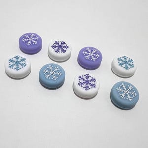 Peut inclure: Huit capuchons de manette ronds en silicone avec des motifs de flocons de neige. Quatre capuchons sont bleu clair avec des flocons de neige blancs, et quatre capuchons sont violets avec des flocons de neige blancs.