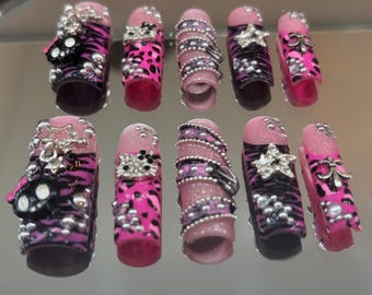 May include: A collection of artificial nails with a variety of designs. The nails feature a combination of pink, black, and silver accents, including zebra stripes, rhinestones, and star-shaped embellishments. Some nails have a pink leopard print.