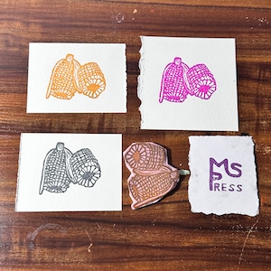 May include: Four different rubber stamps featuring corn on the cob. The stamps are on white card stock. The corn is in orange, pink, gray, and brown. The stamps are arranged in a grid pattern. The bottom right corner of the image shows a white card with the text "MS PRESS" in purple.