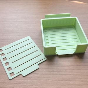 May include: A light green plastic storage box with a removable divider. The box has a rectangular shape and is divided into multiple compartments. The divider is also light green and has a rectangular shape.