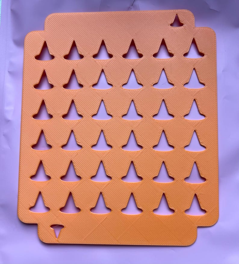 May include: An orange, rectangular organizer with a series of inverted triangle cutouts. The organizer has a textured surface and a small cutout at the top and bottom. The cutouts are evenly spaced and create a grid-like pattern.