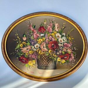 Pu&ograve; includere: Un dipinto incorniciato che raffigura un cesto pieno di fiori colorati, tra cui papaveri rossi, margherite rosa e bianche e fiori selvatici gialli. Il dipinto ha uno sfondo marrone e una cornice dorata.