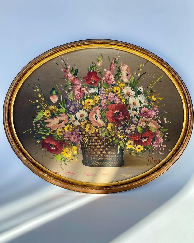 Pu&ograve; includere: Un dipinto incorniciato che raffigura un cesto pieno di fiori colorati, tra cui papaveri rossi, margherite rosa e bianche e fiori selvatici gialli. Il dipinto ha uno sfondo marrone e una cornice dorata.