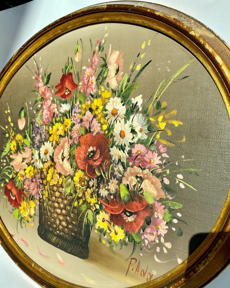 Pu&ograve; includere: Un dipinto incorniciato di un mazzo di fiori colorati in un cesto intrecciato. I fiori includono papaveri rossi, margherite bianche, fiori selvatici rosa e gialli. Il dipinto &egrave; firmato "P.A.V." nell'angolo in basso a destra.